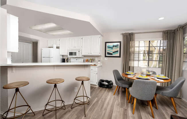 A kitchen with white cabinets and a dining table with grey chairs.