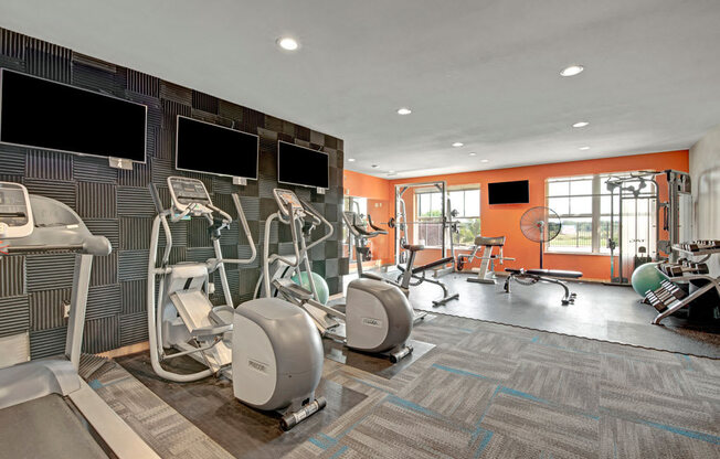 A modern fitness center here at Vue at Pinnacle Park with cardio machines, ellipticals, free weights, strength equipment, wall-mounted TVs, and bright windows for an energizing, well-equipped workout space.
