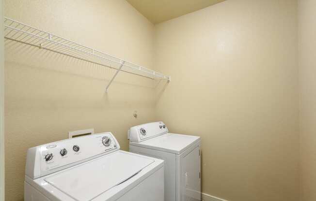 two washers and a dryer in a room with a rack on the wall