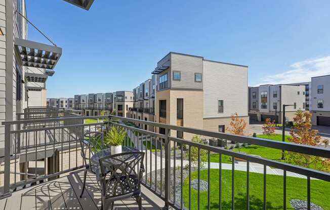 a balcony with a table and chairs overlooking a yard and apartment buildings at Meridian at CityPlace, Woodbury, MN