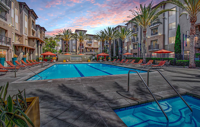 a swimming pool with chaise lounge chairs and umbrellas in front of a building