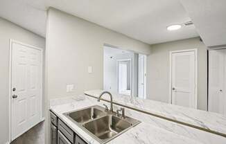 A kitchen with a marble countertop and stainless steel sink.