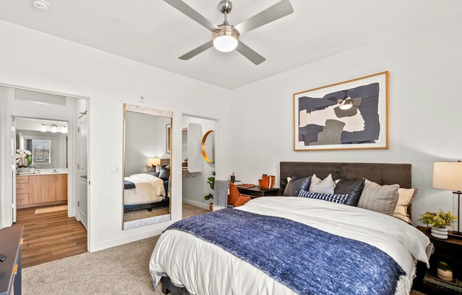 A bedroom with a bed, a ceiling fan, and a painting on the wall.