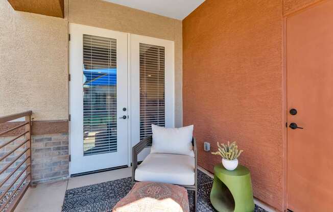 A balcony with a white chair, a green stool, and a white pillow.