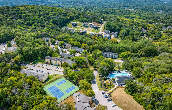A tennis court is surrounded by trees in a residential area.