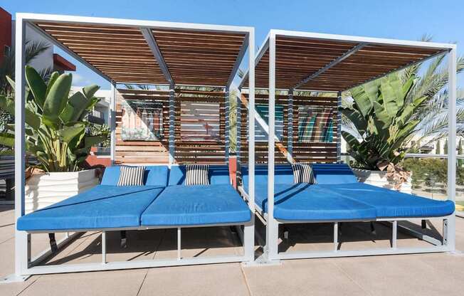 A blue and white daybed with a wooden roof is surrounded by green plants.