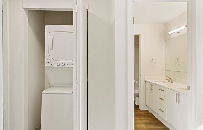 A closet with a white washer and dryer, and the full bathroom to the right with wood flooring.