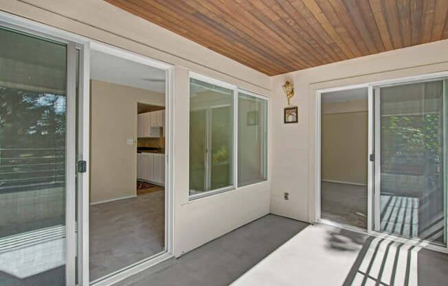 A private covered balcony here at Watercrest with a wood-paneled ceiling and spacious floor area, featuring sliding glass doors and large windows that provide easy access and views into the bright interior living spaces.