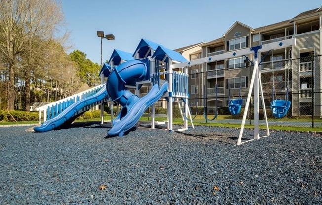 a playground with a blue slide and swings in front of an apartment building