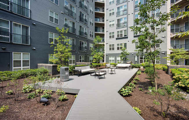 A modern outdoor seating area with benches and trees is surrounded by apartment buildings.