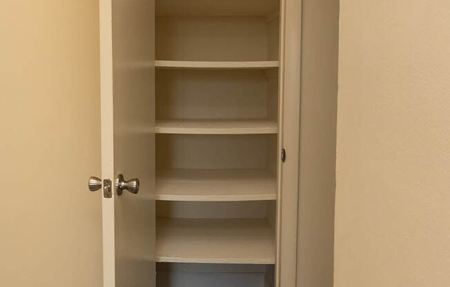 A white door with a handle is open to a hallway with shelves.
