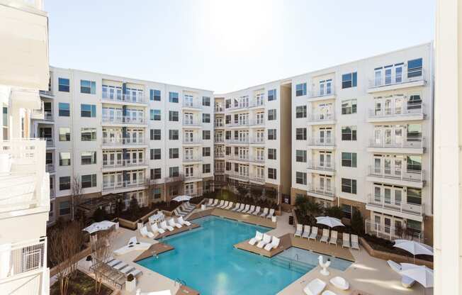 an overhead view of a large pool with white lounge chairs and umbrellas in front of