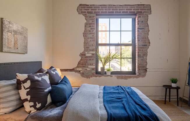 a bedroom with a exposed brick wall and a bed with a blue blanket and pillows at The 22 Apartments, Missouri