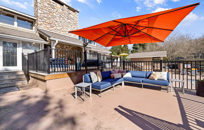 a patio with an orange umbrella and couches in front of a house