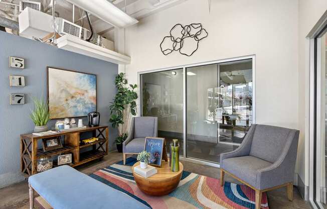 A modern living room with a grey sofa, a grey armchair, a wooden coffee table, and a large painting on the wall.