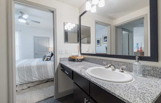 a bathroom with a sink and mirrors and a bedroom with a bed