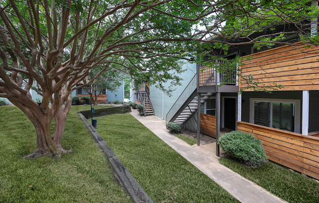 Exterior view of building with sidewalk winding through lush grass and trees