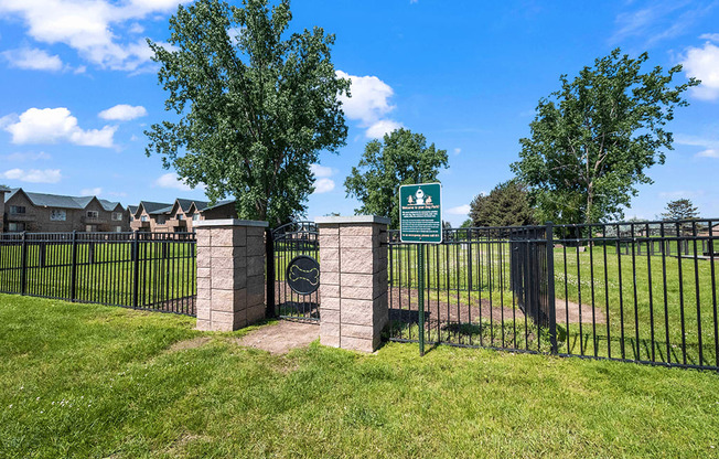 A green sign is on a gate in front of a grassy area.