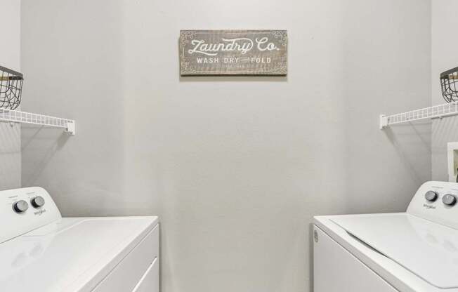 Two white washing machines in front of a sign that says "Tauntry Co. Wash Dry Fold".