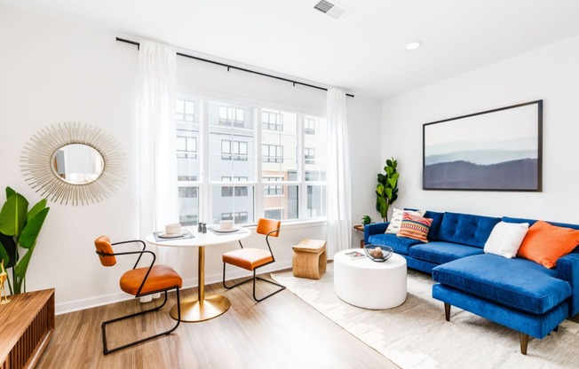 a living room with a blue couch and a round table and a large window at One Ten Apartments, New Jersey