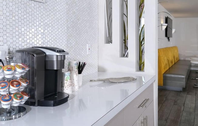 Fifteen 50 apartments Las Vegas clubhouse coffee corner with Keurig and coffee cups on counter with modern white penny tile backsplash.