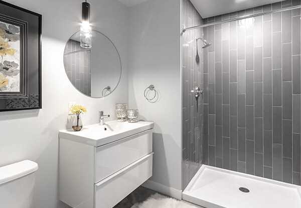 Steelcote Crossing bathroom with white cabinetry, white quartz countertops, large circular mirror and walk in shower with tile surround at Steelcote Square, Missouri