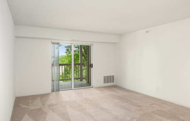 an empty living room with a sliding glass door to a balcony