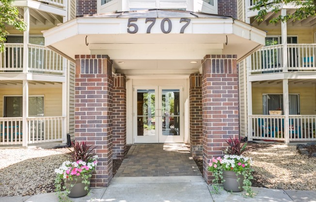 the front entrance of a condo building with flowers on the sidewalk