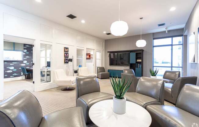 A white table with a plant on it sits in the middle of a room with grey couches.