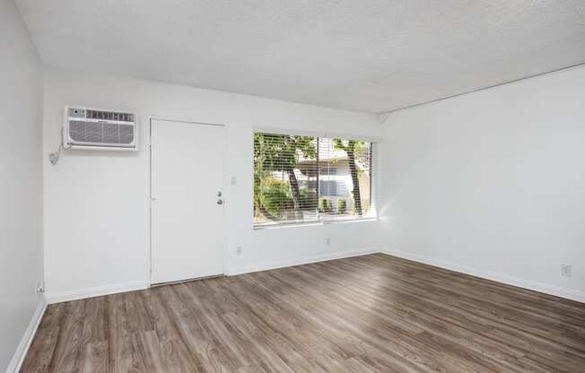 an empty room with white walls and wood flooring and a window