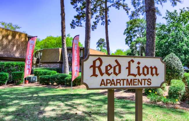 a red lion apartments sign in front of a yard with trees