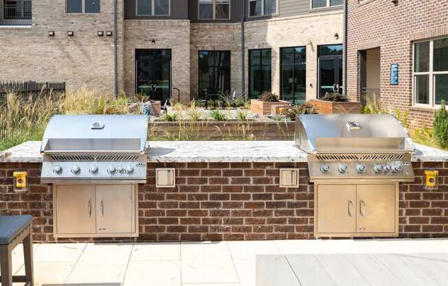 two stainless steel barbecue grills in front of a brick wall