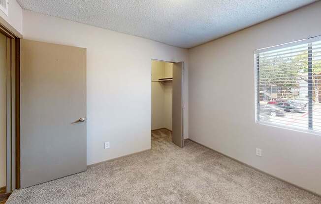 A room with a carpeted floor, a door, and a window with blinds.