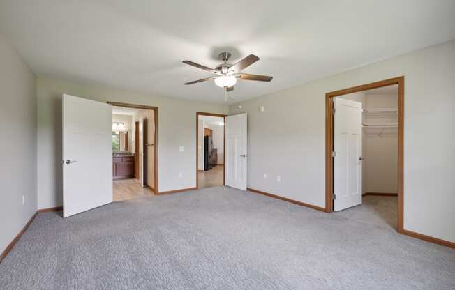 an empty living room with a ceiling fan and doors to a bedroom and a bathroom