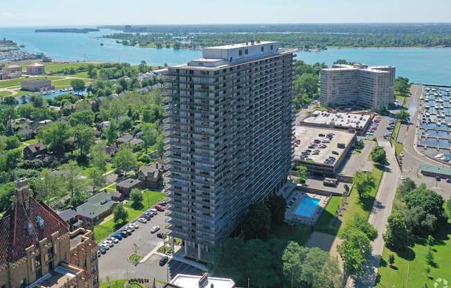 Exterior of the Jefferson. The building stands 30 stories tall. The building is located on the Detroit River. There are green trees and roadways around the building.
