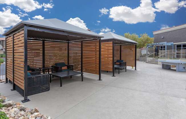 A wooden structure with a black roof and a table and chairs in front of it.