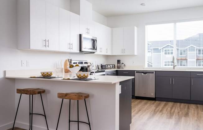 a kitchen with white cabinets, breakfast bar with two stools in front of it