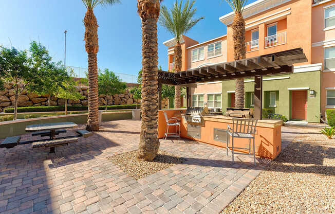 A patio with a table and chairs under a pergola with palm trees in the background.