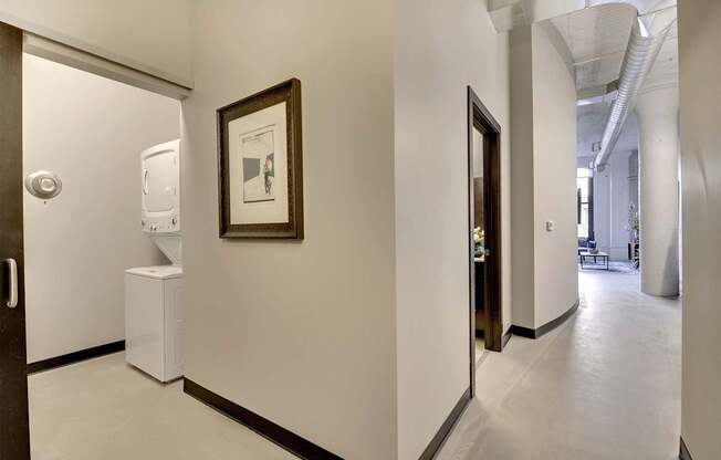 A hallway with a framed picture on the wall and a white trash can.