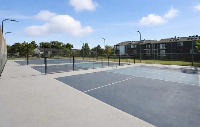A tennis court surrounded by a fence and apartment buildings.