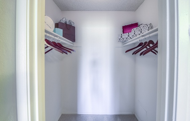 A white closet with clothes hanging on the shelves.