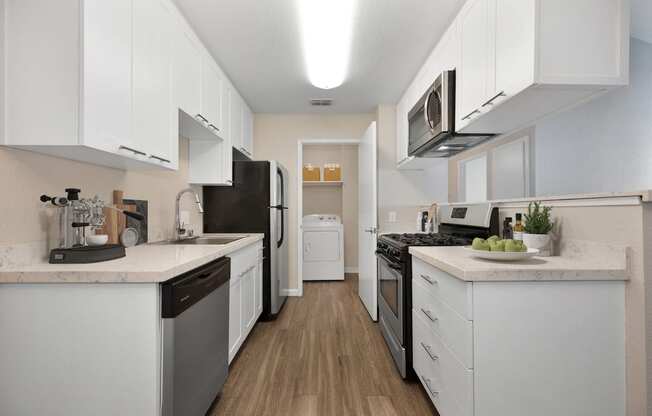 a spacious kitchen with white cabinets and stainless steel appliances. Closet at the end of the kitchen includes a full size washer and dryer with shelving above.