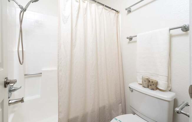 A white bathroom with a toilet, shower curtain, and towel rack.