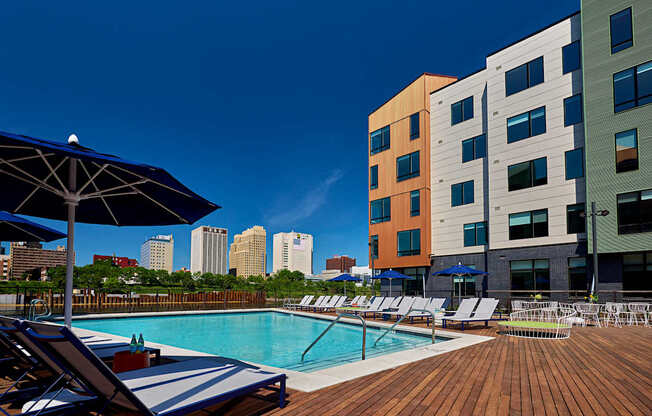A pool area with chairs and umbrellas in front of a multi-story building.
