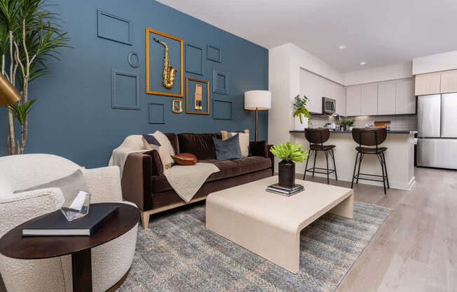 A living room with a brown sofa, a white armchair, a coffee table, and a plant.