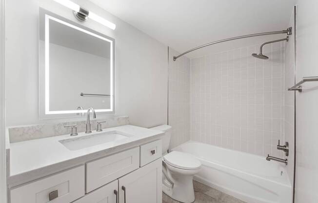 A white bathroom with a sink, mirror, toilet and bathtub.