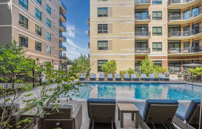 A pool surrounded by chairs and a building in the background.