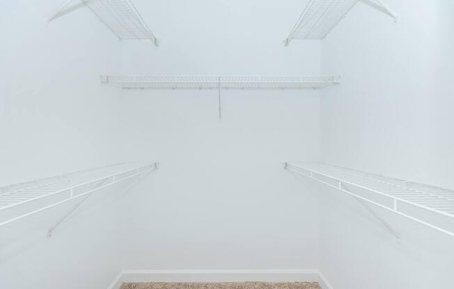 Empty closet with white wire shelving along the walls, no items or decorations present, featuring light-colored walls and a soft carpeted floor.
