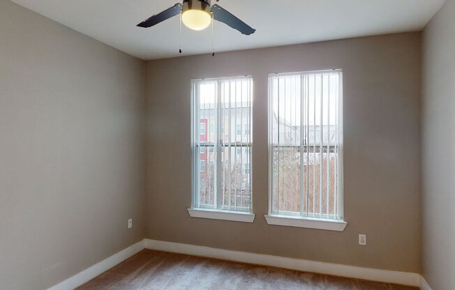 A room with a ceiling fan and two windows.