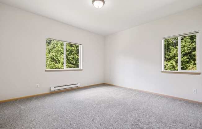 A bedroom with a carpeted floor and two windows at The Madison Apartments in Olympia, WA